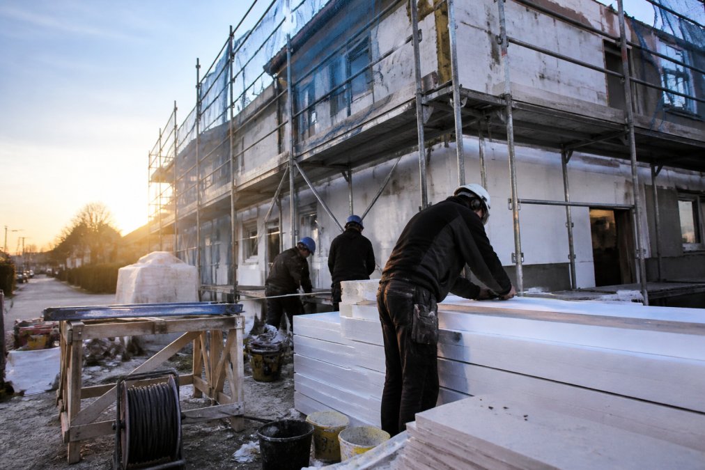 Werkteam op de werf met bouwmaterialen en gereedschap, voorbereiding van isolatiewerken aan een gevel met steigers en beschermingsnetten in de vroege ochtend