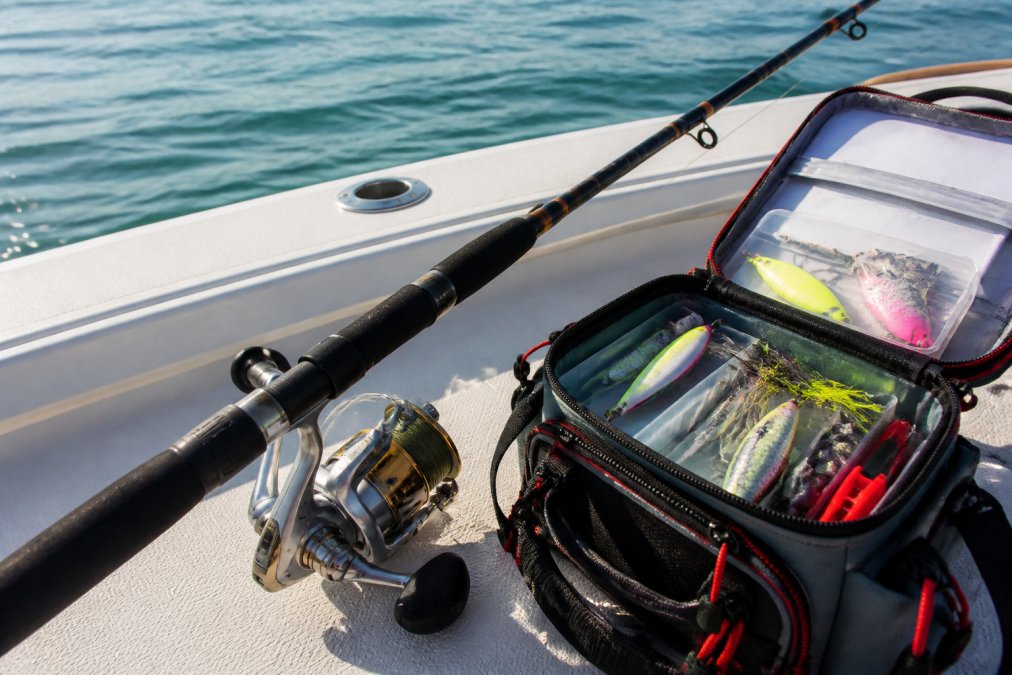 A fishing rod and reel setup laid out on a boat deck with a tackle bag open nearby, showing lures and terminal tackle ready for use on a sunny Gulf Coast morning