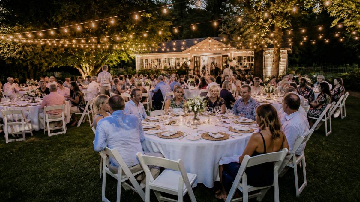Guests dining at a backyard garden party featuring elegant tables and chairs rented for the event.