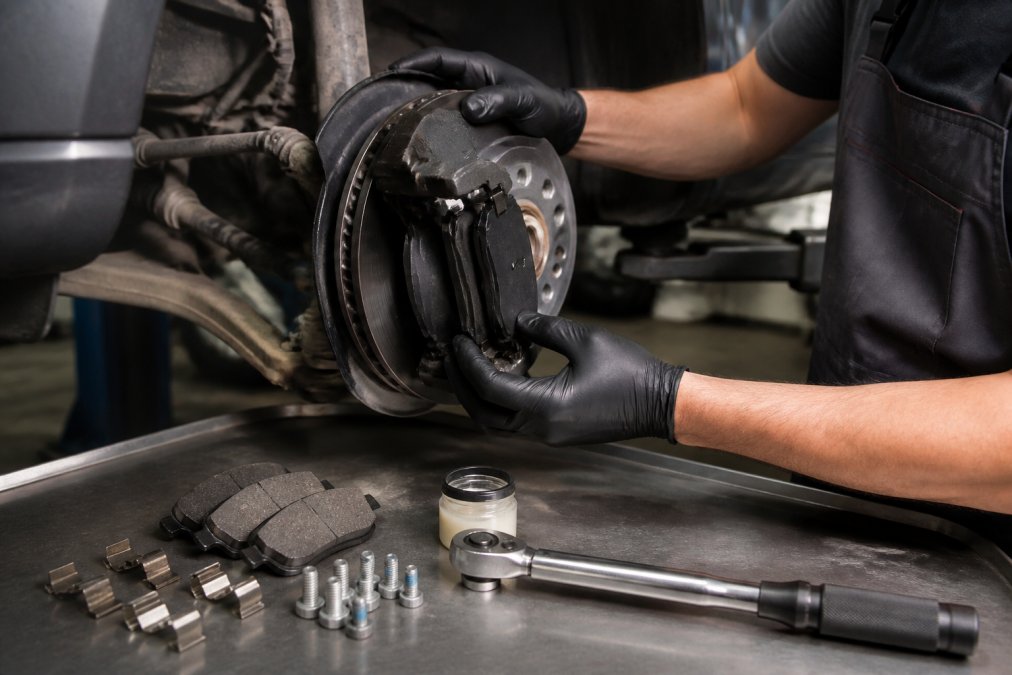 Mechanic using a torque wrench to replace brake pads on an Audi Q5 caliper assembly with new hardware and lubricant