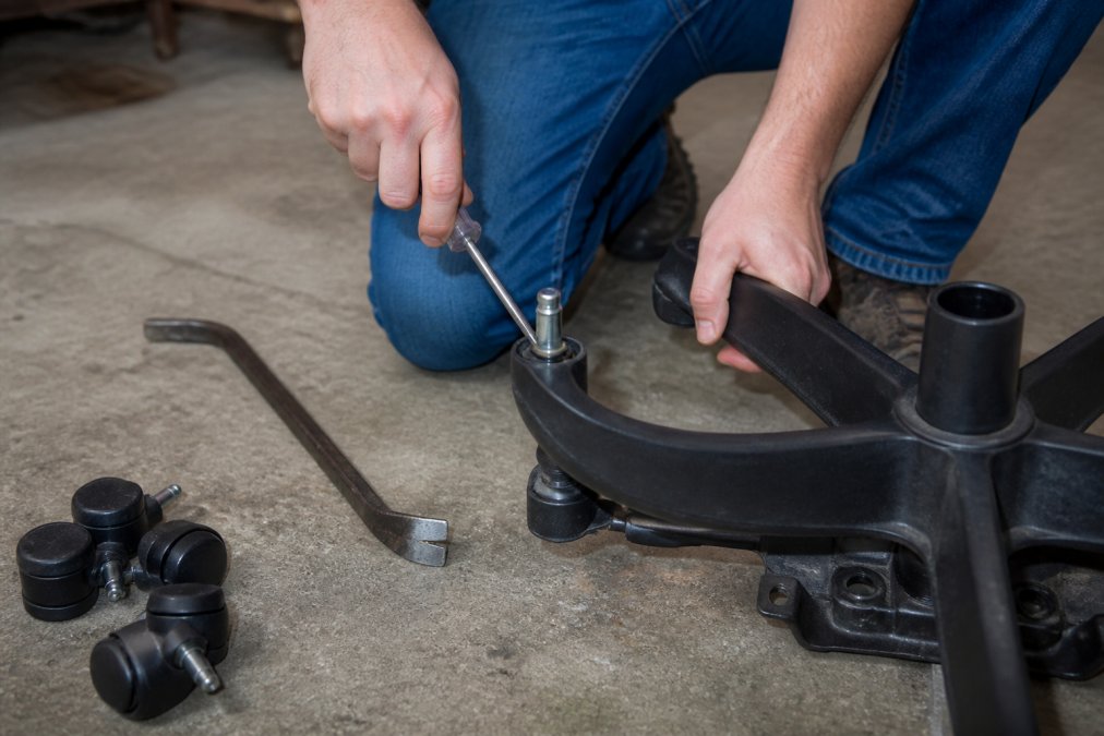 Using a flathead screwdriver to pry a stuck wheel from an office chair base while replacing casters