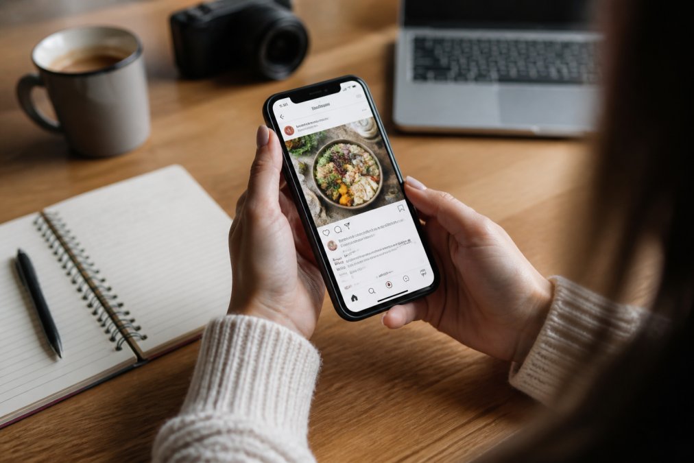 Close-up of hands holding smartphone displaying Instagram feed with high-engagement reposted content and affiliate links visible on screen, natural indoor lighting