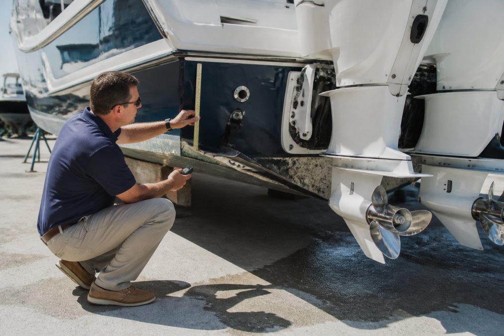 Experienced marine surveyor examining the transom and hull structure of an offshore fishing yacht during a pre-repower assessment, using measurement tools and inspection equipment in bright daylight