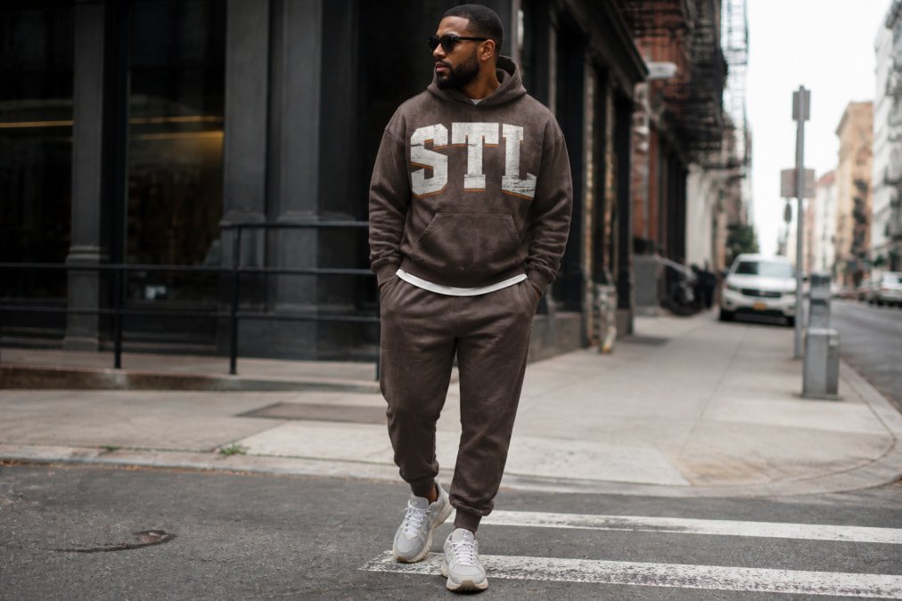 Urban professional wearing oversized boxy hoodie and tapered sweatpants on a city street, showcasing layered streetwear styling with minimalist aesthetic and natural daylight