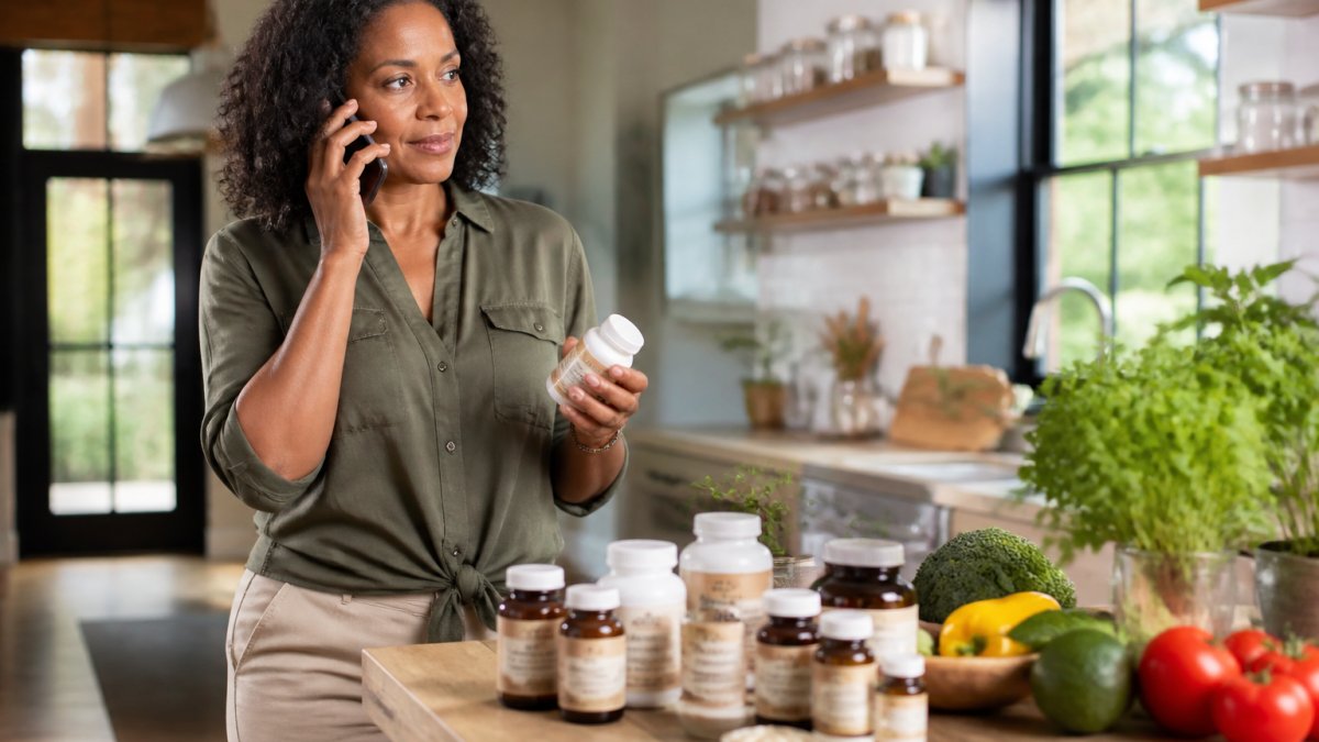 Close-up of various supplement bottles and capsules arranged on a wooden surface with fresh herbs and vegetables in soft natural light