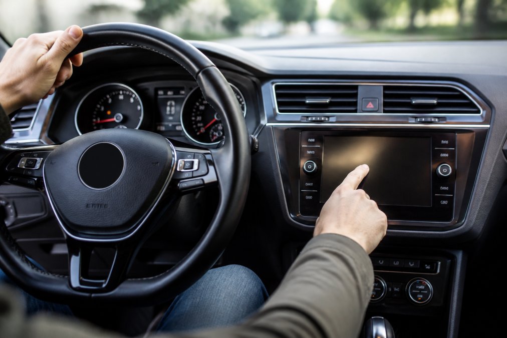 Close-up of a VW steering wheel with hands navigating the infotainment touchscreen menu while seated in the driver's position, showing the dashboard display