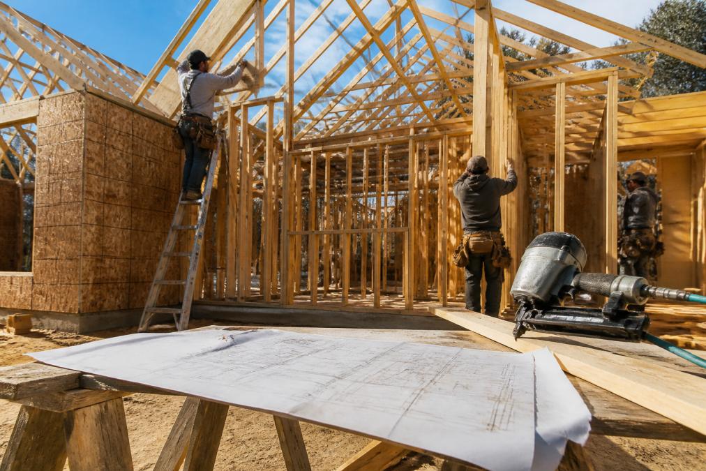 Framing crew installing wood studs and roof trusses for residential framing with construction blueprints nearby