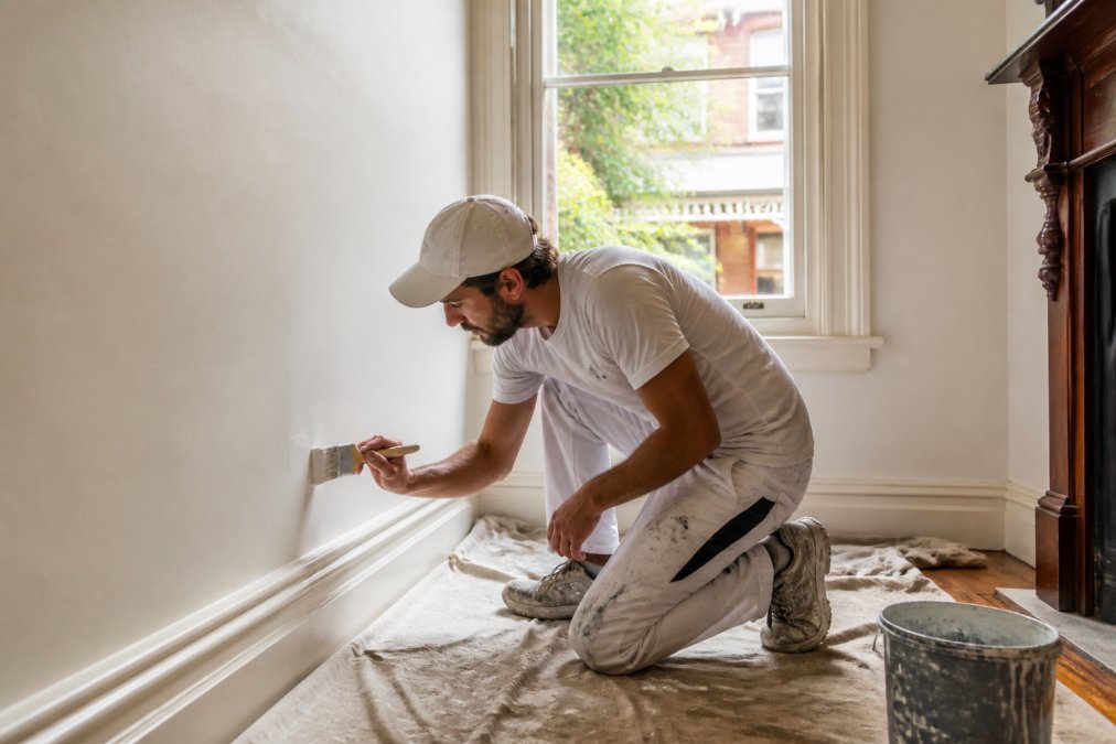 Professional painter in a heritage-style home in Sydney's Inner West carefully cutting in along a wall with a brush, drop sheets protecting the timber floorboards, natural daylight streaming through a sash window