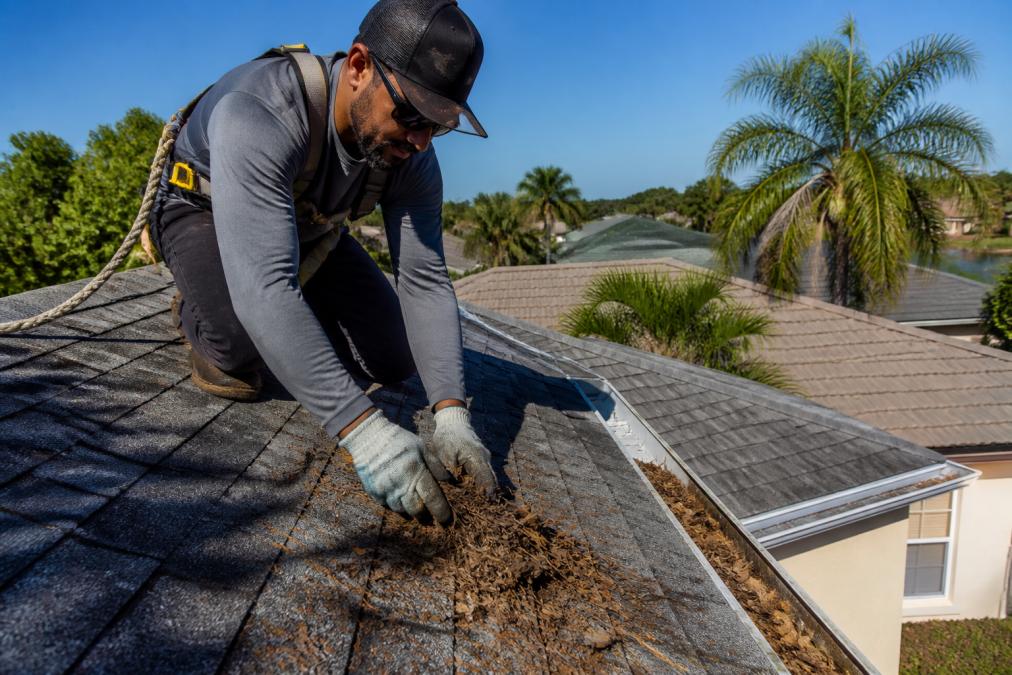 Professional demonstrating safe debris removal from residential roof with proper safety equipment and harness on Florida home