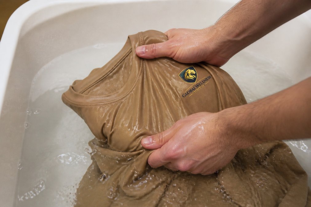 Close-up of hands washing athletic apparel in cold water, showing proper care technique to preserve fabric durability and moisture-wicking properties