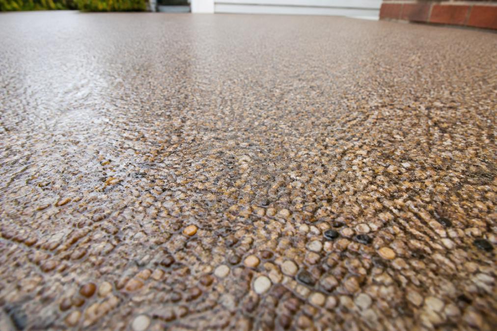 Close-up of finished resin bound driveway surface showing smooth, seamless texture with natural stone aggregate in warm earth tones, water droplets visible on the surface demonstrating water drainage