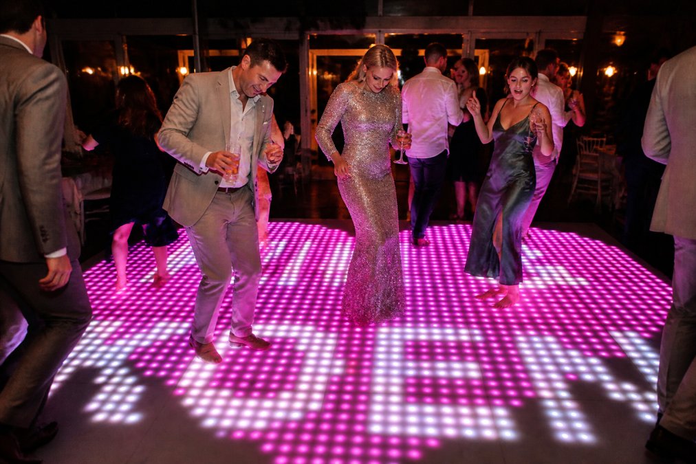 Close-up van dansende gasten in feestkleding op een verlichte dansvloer met levendige LED-kleuren en pixelpatronen duidelijk zichtbaar onder warme feestverlichting