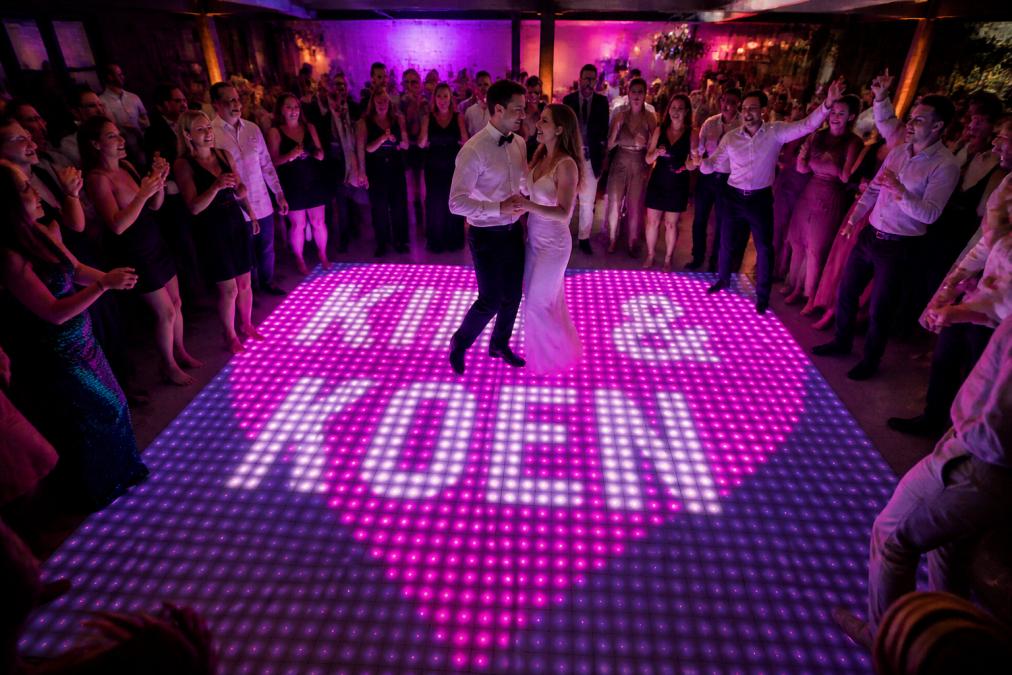 Groep feestgangers dansend op een grote verlichte dansvloer in een zaal, met verschillende LED-kleuren zichtbaar en mensen in feestkleding die plezier hebben