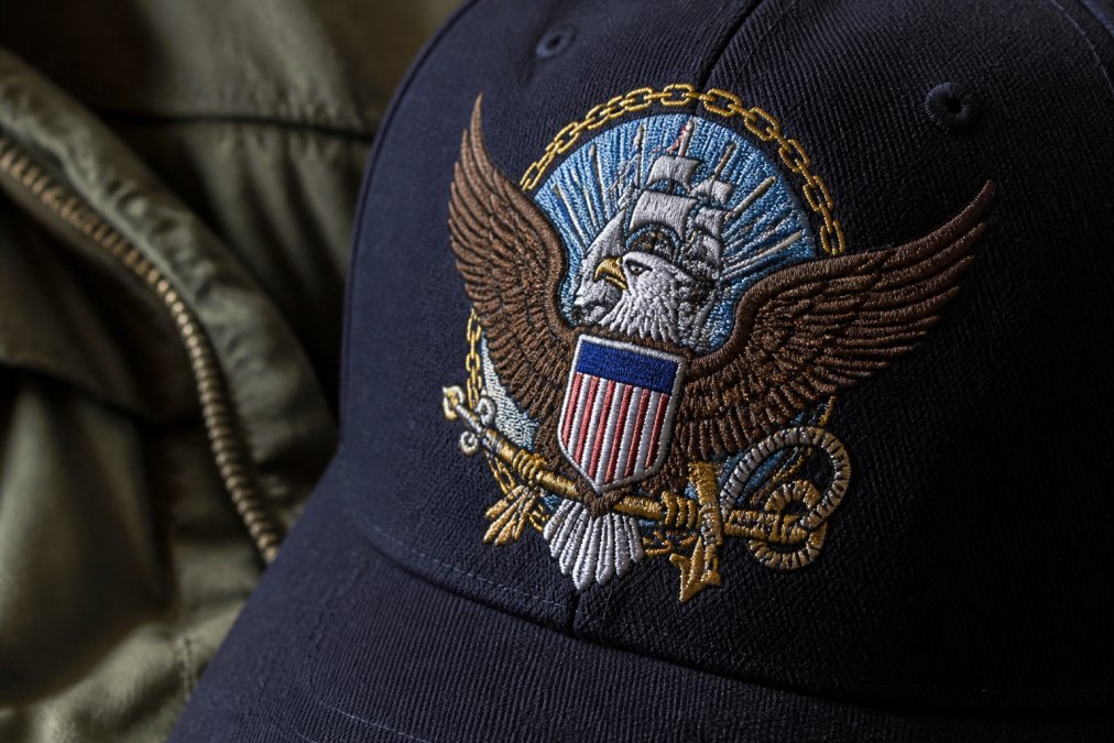 Close-up of embroidered military insignia on cotton twill cap showing intricate stitching detail, thread colors representing service branch identity, and professional embroidery craftsmanship with natural lighting highlighting texture