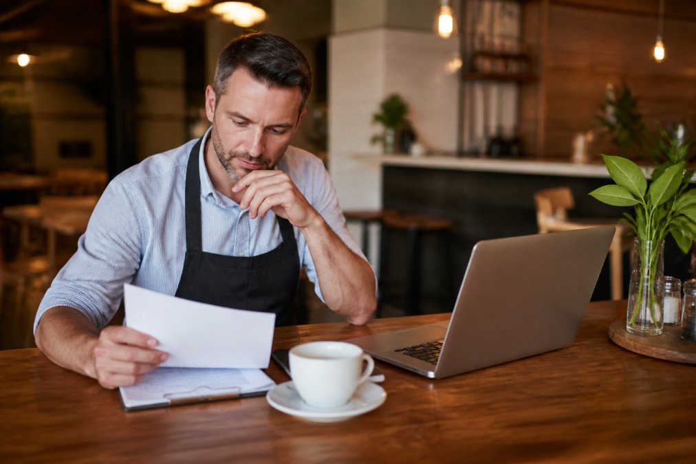 Restaurant owner reviewing email marketing automation templates on a laptop at a wooden counter