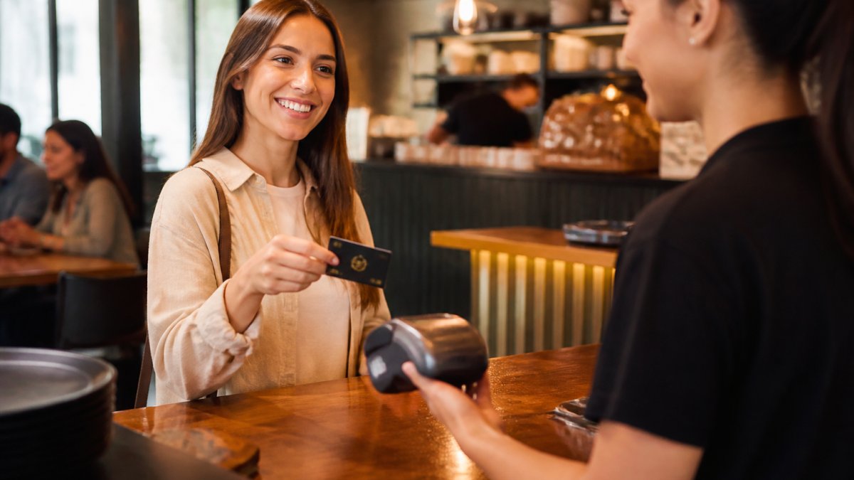 Smiling customer at restaurant counter showing membership card or phone to cashier while making a purchase, warm lighting, friendly interaction
