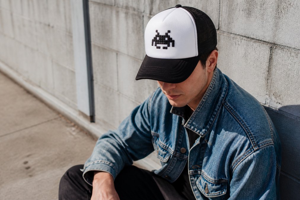 Close-up van iemand die een gaming-gerelateerde trucker cap draagt met casual streetwear ensemble, inclusief vintage elementen. Moderne, verzorgde look. Natuurlijke verlichting buiten