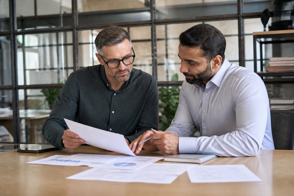 Business owner reviewing financial documents and growth metrics with a financial advisor in a professional office setting, natural lighting