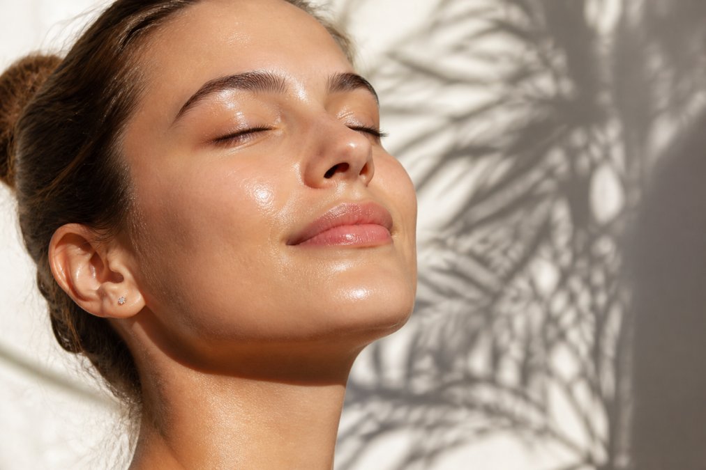 Close-up of a person's glowing, hydrated complexion with visible skin luminosity and smooth texture in natural daylight, showing the radiant effect of brightening serum