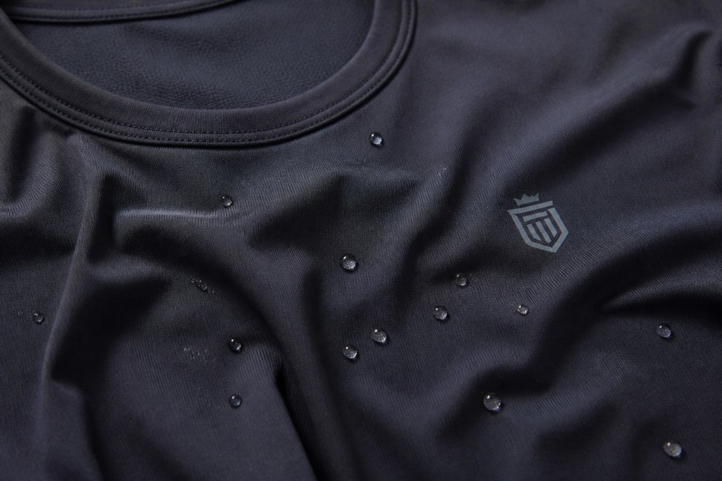 Close-up of premium athletic fabric textures showing soft hand-feel and technical weave, with water droplets demonstrating moisture-wicking properties on DreamKnit material