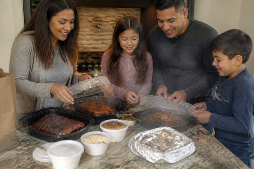 A family unpacking steaming grilled meats and ribs from El Gordo's Grill, a hearty Rib City alternative.