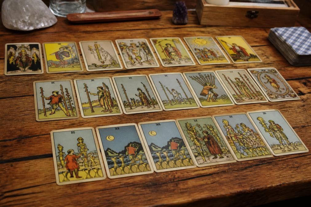 Spread of tarot cards displayed on a wooden table showing Major and Minor Arcana cards with distinctive symbolic artwork and archetypal imagery visible