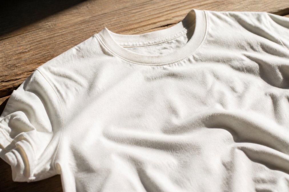 Close-up of a soft, well-worn white cotton t-shirt laid flat on a wooden surface, showing the smooth fabric texture in warm natural light