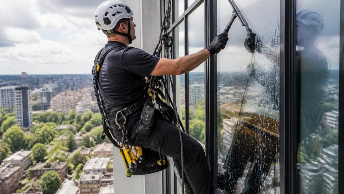 Rope access technician using safety harness for working at height cleaning on a high-rise building facade.