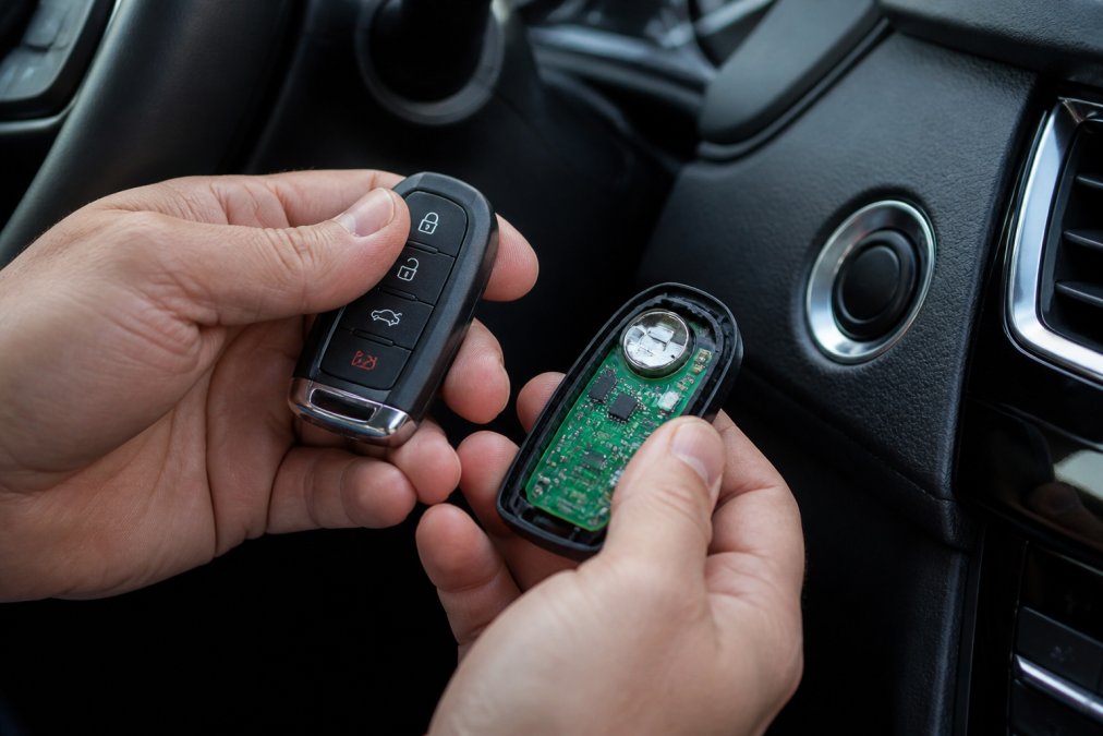 Close-up of a person's hands holding a modern car key fob near a car's push-to-start button, showing the intricate internal circuit board and buttons