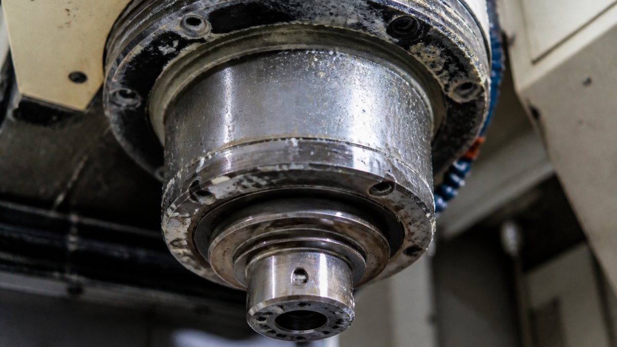 Close-up of a CNC machine spindle showing accumulated dust, coolant residue buildup, and visible wear on bearing surfaces from extended periods without cleaning or lubrication