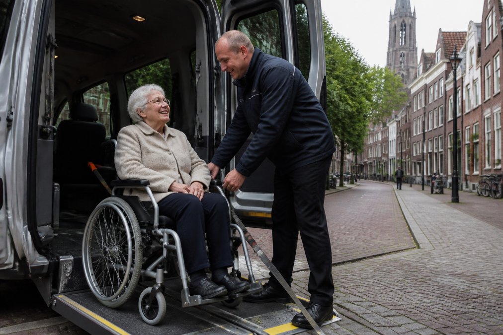 Vriendelijke chauffeur helpt lachende passagier in rolstoeltaxi bij een reservering annuleren in Utrecht