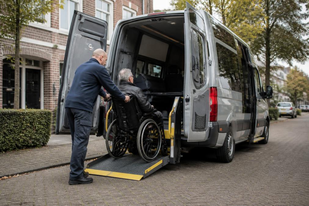 Gespecialiseerde rolstoeltaxi met geopende hydraulische rolstoellift op een rustige straat in Utrecht, waarbij een professionele chauffeur een passagier voorzichtig helpt in te stappen