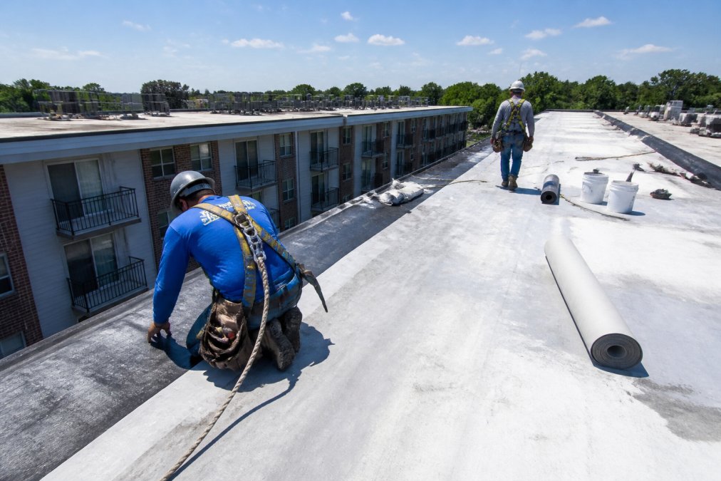 Commercial roofing crew using safety harnesses to inspect a flat membrane roof on an apartment building