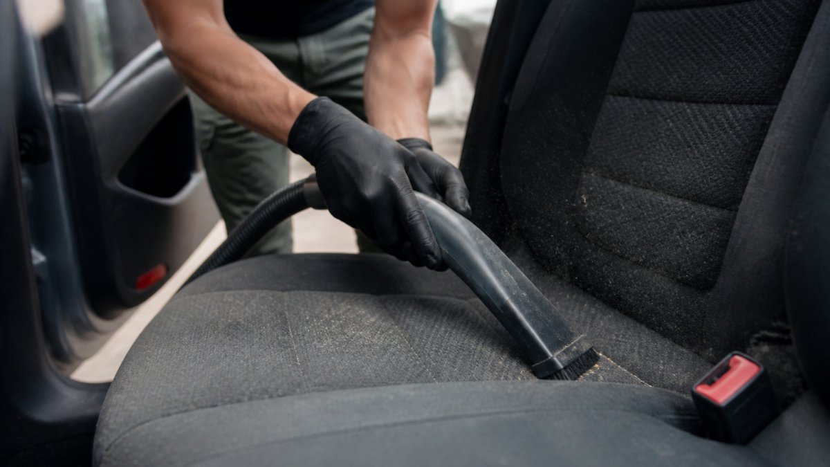 Iemand die met een handstofzuiger grondige aandacht aan de stoffen autobekleding besteedt, zichtbare stofdeeltjes en vuil worden opzogen uit de naden van zetels