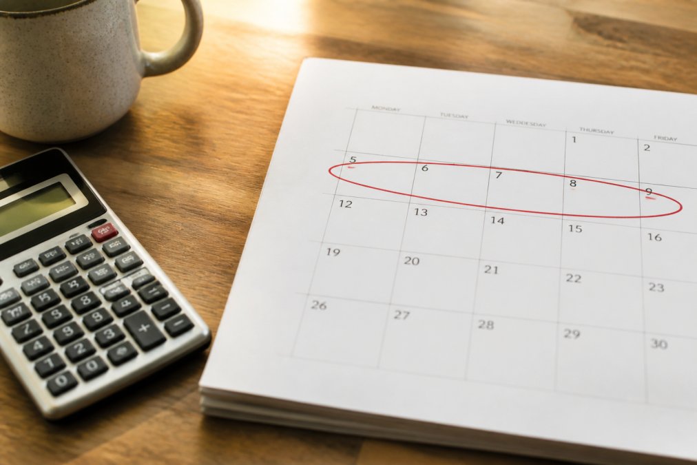 Close-up of a paper calendar with a five-year span circled in red pen, sitting beside a financial calculator and a ceramic coffee mug on a wooden desk in soft morning light