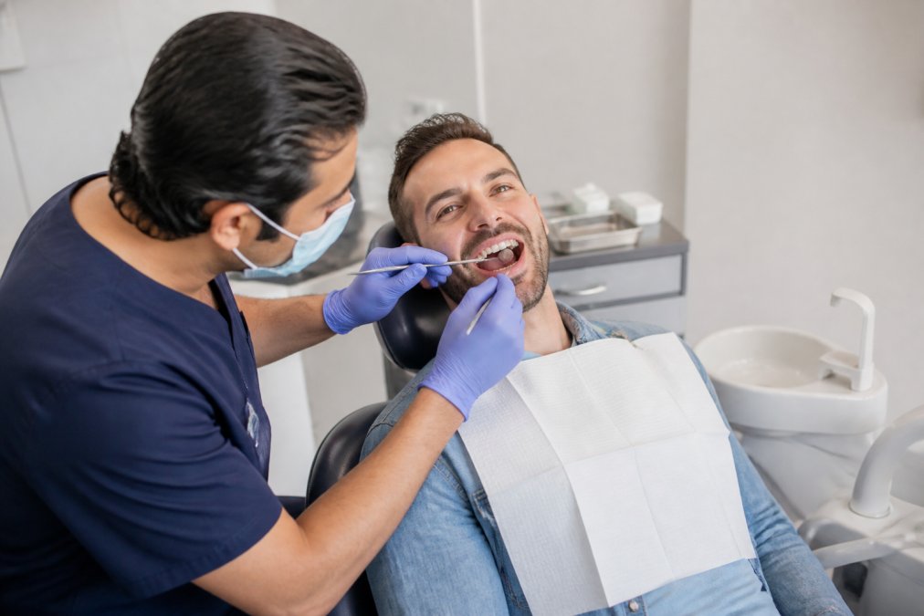 Dental professional examining patient's teeth and gums during routine checkup, patient reclined in modern dental chair in bright, clean surgery with overhead lighting