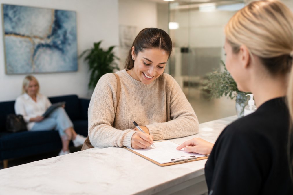 Calm, welcoming dental reception area with comfortable seating, patient filling out health form at desk with pen in hand