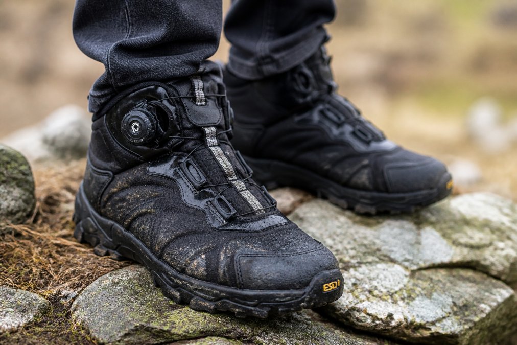 Close-up of weathered leather hiking boots on rocky terrain, showing waterproof construction and durable wear patterns from real field use