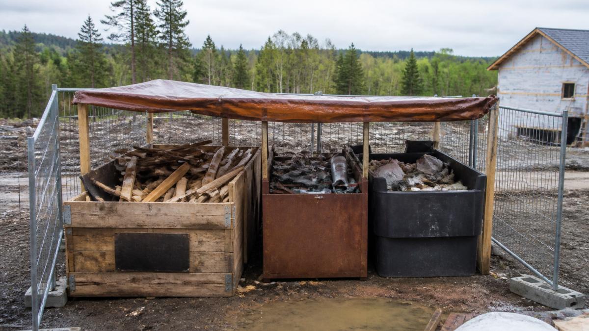 Labeled bins for rural construction waste stored behind a fence to prevent wildlife access and rain damage.
