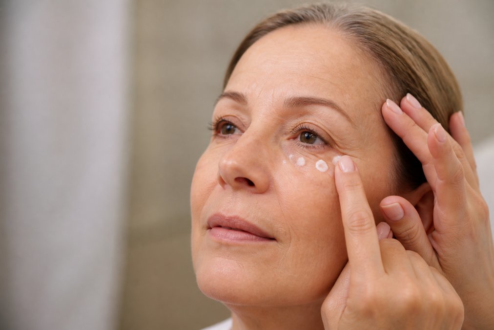 Primer plano de manos aplicando delicadamente contorno de ojos en la zona periocular de una mujer madura