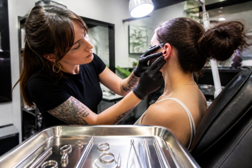 Professional piercer examining a client's ear anatomy in a sterile studio for safe body piercing