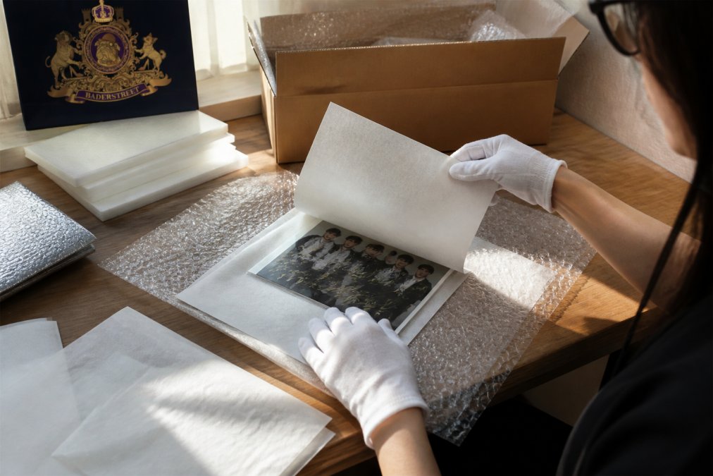 Professional carefully wrapping a hand-signed K-pop autograph in acid-free tissue paper, surrounded by bubble wrap, foam sheets, and protective materials on a wooden workbench with natural lighting