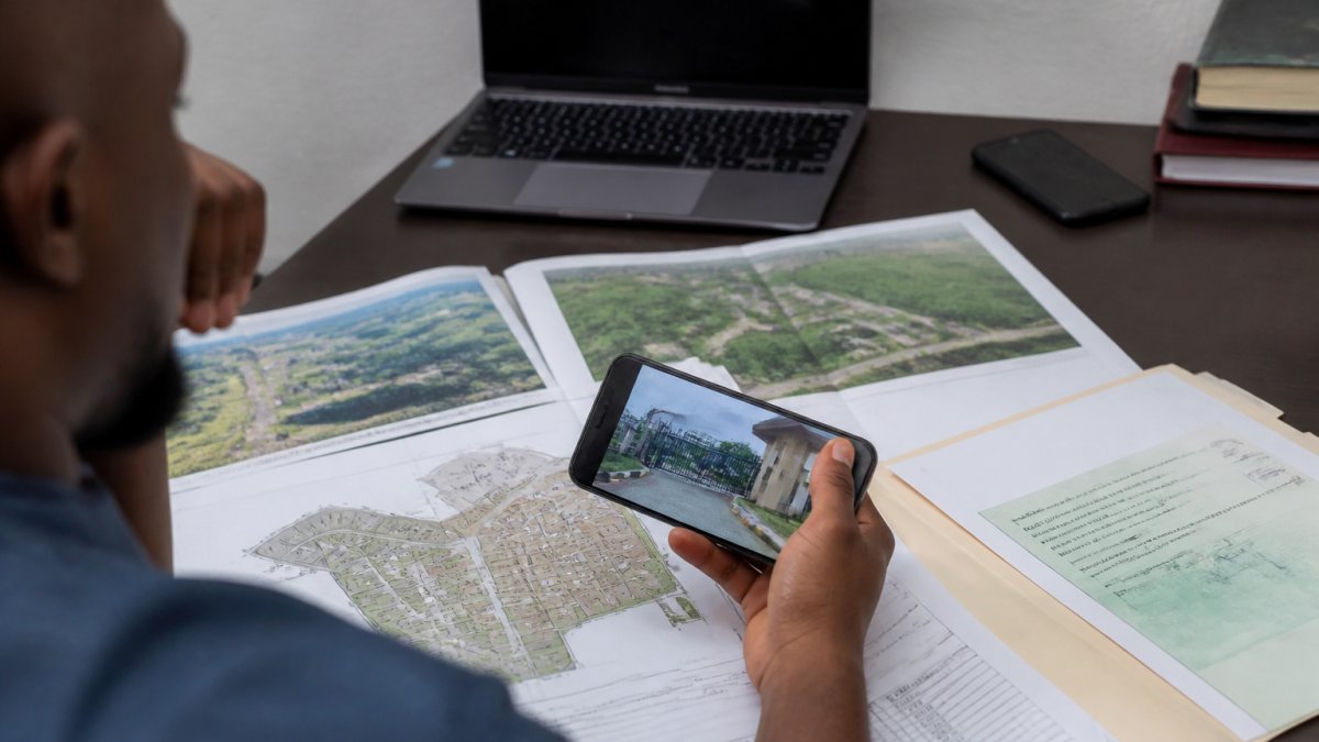 Professional reviewing property documents and survey plans at a desk with a laptop and mobile phone showing property details