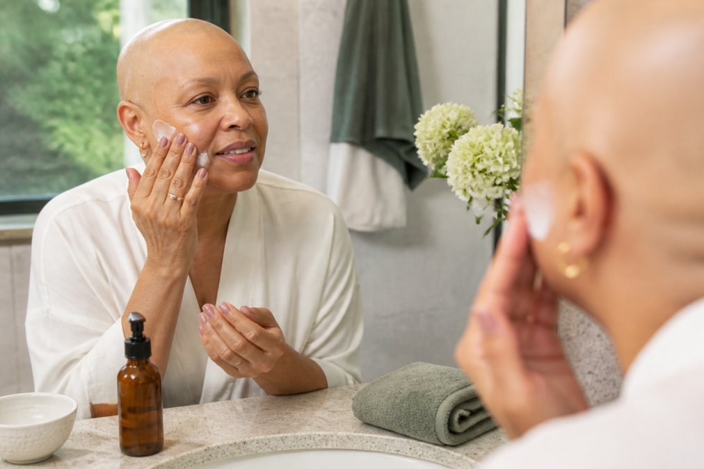 Woman gently applying fragrance-free safe skincare cream to her cheek in soft morning light