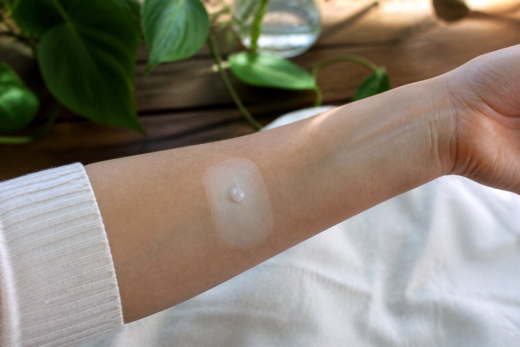 Close-up of a person's inner arm showing a small amount of skincare product applied to a clean, pale test area for patch testing, with natural daylight illuminating the skin