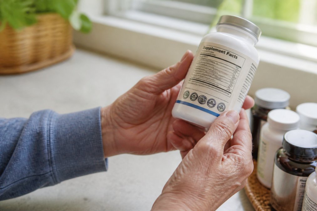 Close-up of hands holding a supplement bottle, carefully examining the label and third-party testing certification marks in bright natural lighting