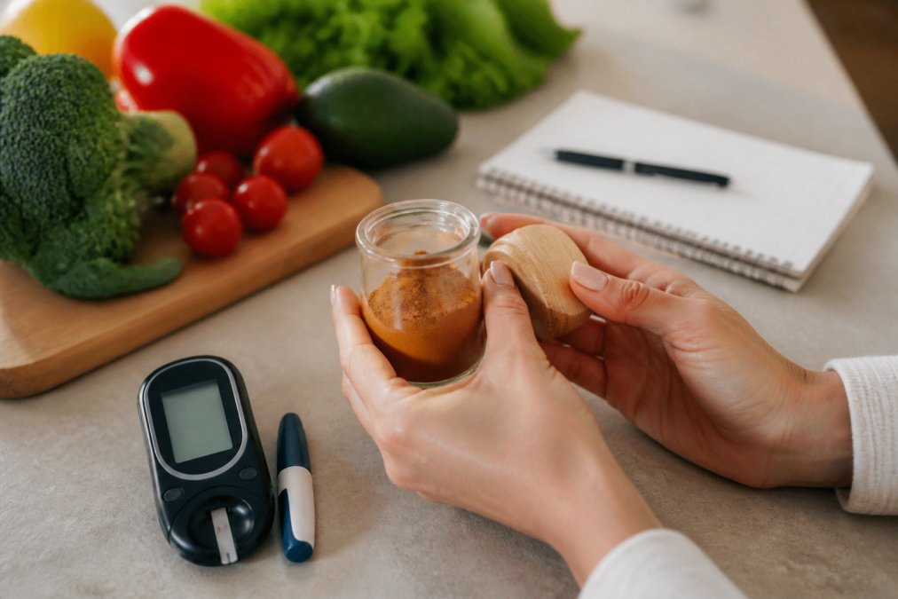 Hands holding cinnamon near a glucose meter and vegetables to find safe supplements for blood sugar management.