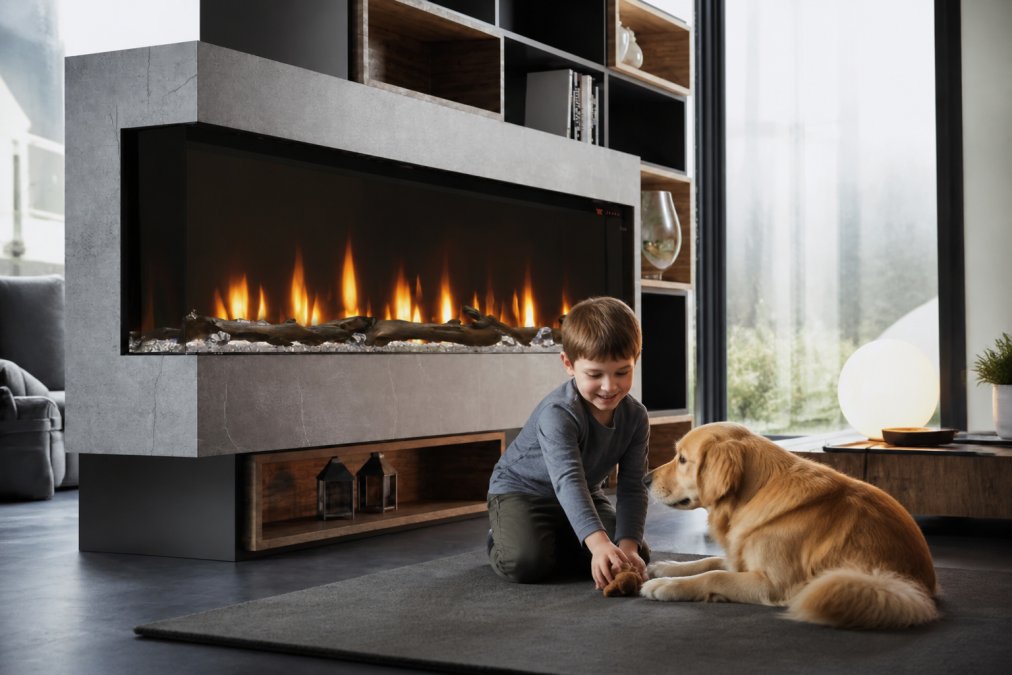 Young child and golden retriever playing safely near a modern electric fireplace with protective glass barrier visible, warm ambient glow illuminating a family living room with contemporary furniture