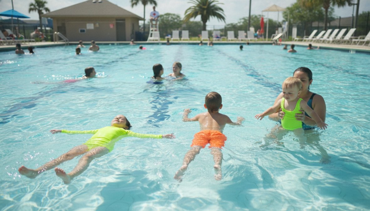 Children wearing bright neon yellow and neon orange swimsuits playing in a crystal-clear pool, clearly visible from above and at water level during daytime
