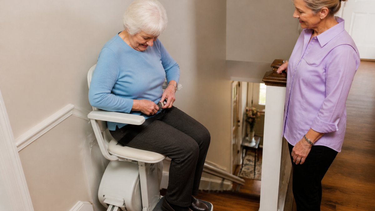 Caregiver assisting an older adult fastening a seat belt on one of our steep stair lifts at home.